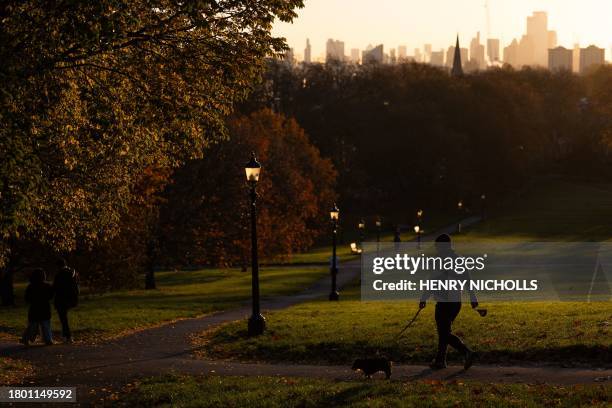 Person walk with a dog in Primrose Hill as the sun rises in London, on November 25, 2023.