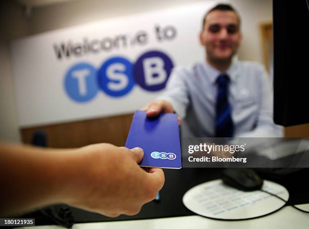 Customer, left, passes their savings book to an employee in this arranged photograph inside a newly rebranded branch of TSB, part of the Lloyds...