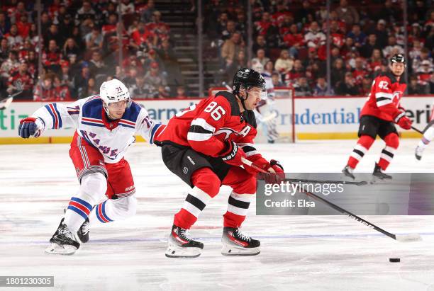 Jack Hughes of the New Jersey Devils takes the puck as Tyler Pitlick of the New York Rangers defends during the first period at Prudential Center on...