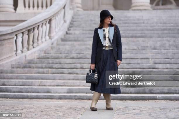 Gabriella Berdugo wears a full Dior look, a black hat, a navy /dark blue blazer jacket with pale / light blue lapels, a black and white striped wool...