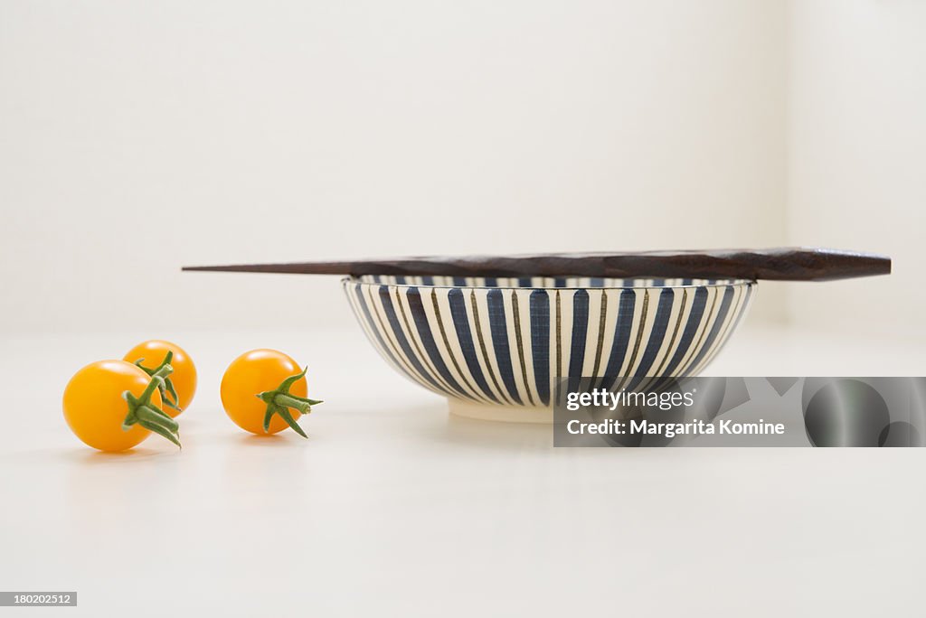 Three yellow tomatoes and a bowl with chopsticks