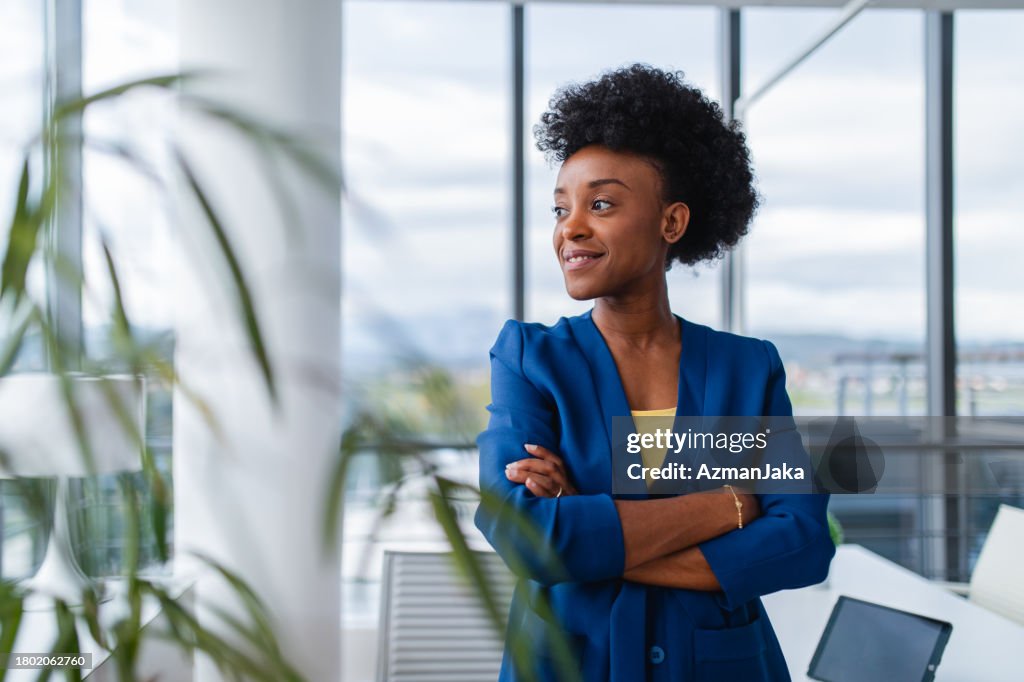 Confident Black Female Businesswoman Looking Out The Window With Her Arms Crossed