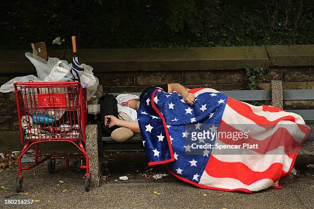 Homeless man sleeps under an American Flag blanket on a park bench on September 10, 2013 in the Brooklyn borough of New York City. As of June 2013,...