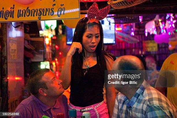 Young Thai ladyboy waitress, smiles and flirts with two western customers in a bar at Patong Beach, Phuket island. Patong's pulsating nightlife never...