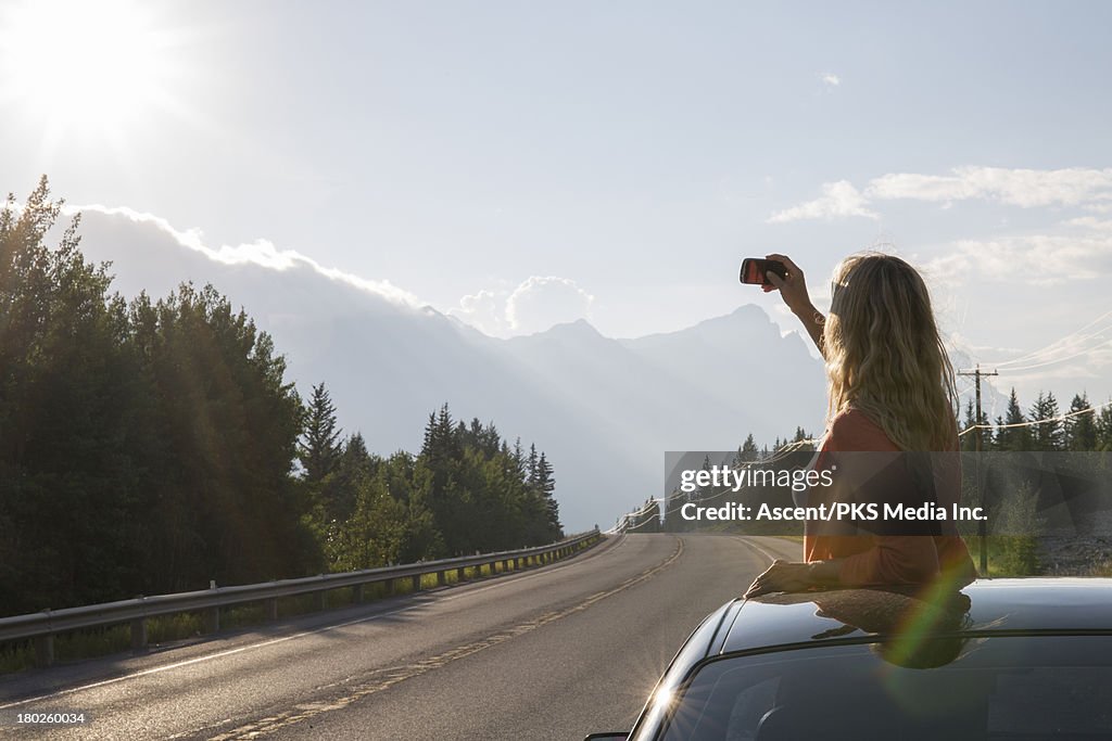 Woman takes picture through car's roof, of sunrise