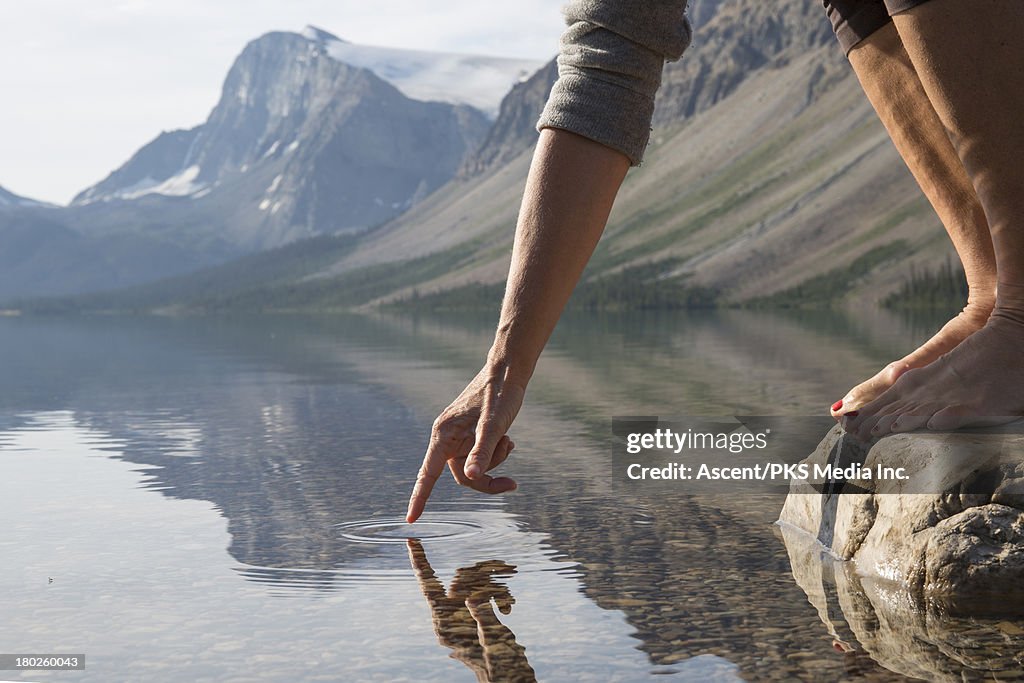 Woman's hand touches water surface, mtn lake