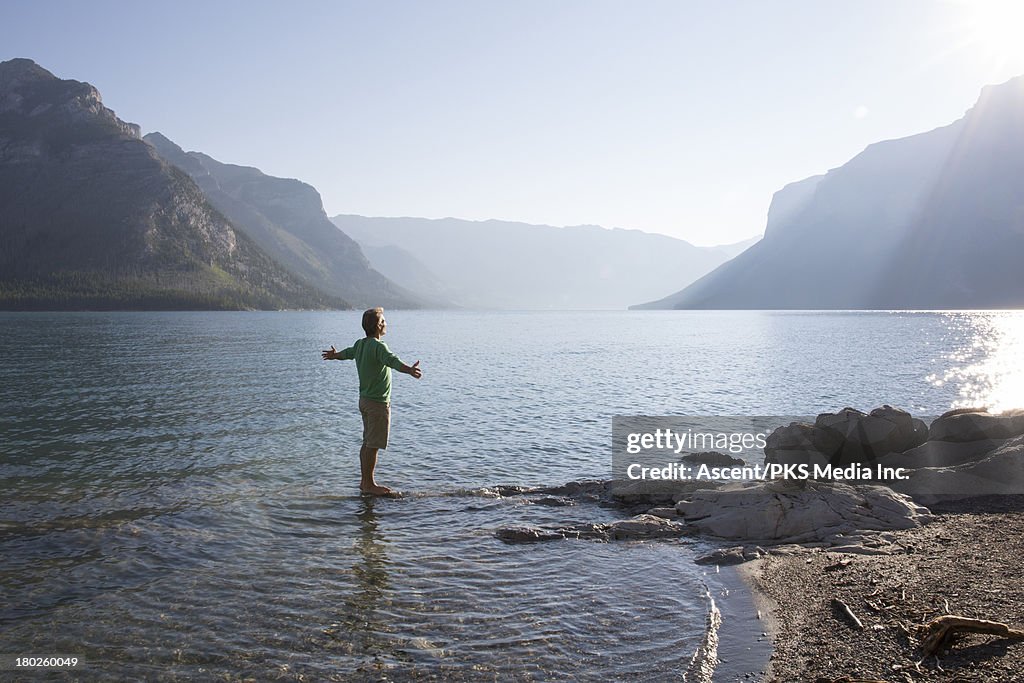 Man stands in mountain lake, arms outstretched