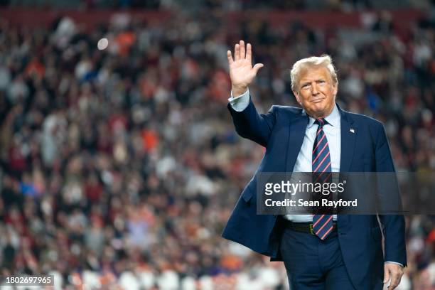 Former U.S. President Donald Trump waves to the crowd on the field during halftime in the Palmetto Bowl between Clemson and South Carolina at...