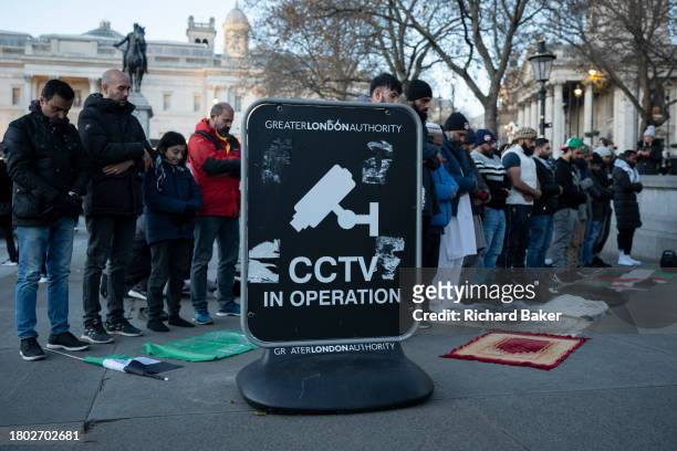 As pro-Palestinian supporters march again through central London to demand a permanent ceasefire in Gaza, muslim men pray next to a warning of CCTV...