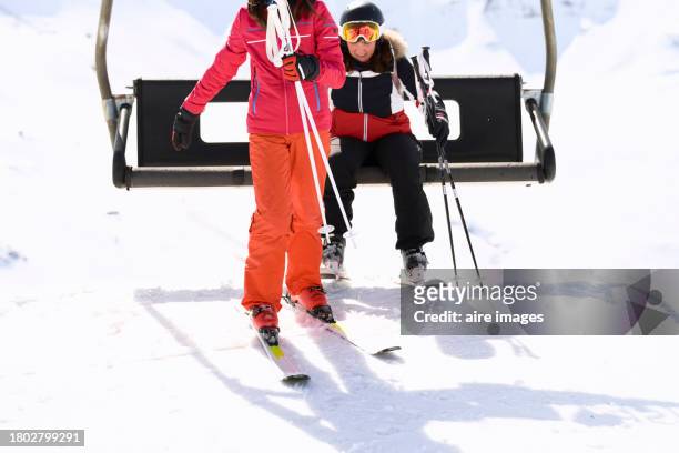 a woman and a teenage girl getting off the chair lift to ski, they are wearing their ski clothes, the teenage girl is seen from the shoulders down and the woman is sitting in the background, the mountain is covered with snow. - woman on ski lift stock pictures, royalty-free photos & images