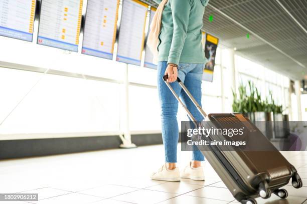 close-up of the legs of a woman in casual clothes standing with her suitcase looking at the airport board, side view - human role stock pictures, royalty-free photos & images