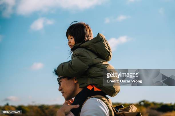 joyful asian toddler girl riding on father’s shoulders against blue sky - nepal celebrates kuse aunsi or fathers day for departed souls stock pictures, royalty-free photos & images