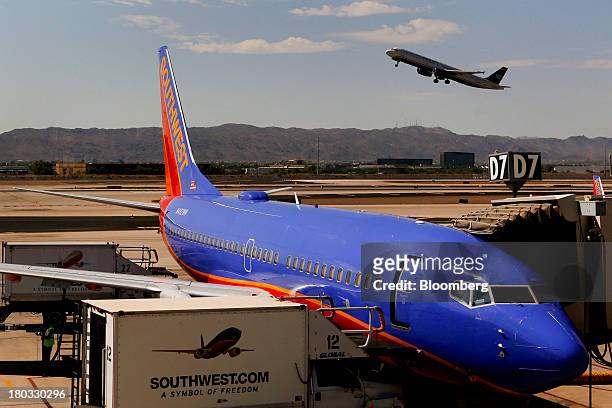 Southwest Airlines Co. Boeing 737-7H4 plane sits at a gate as a US Airways Group Inc. Jet takes off from Phoenix Sky Harbor International Airport in...