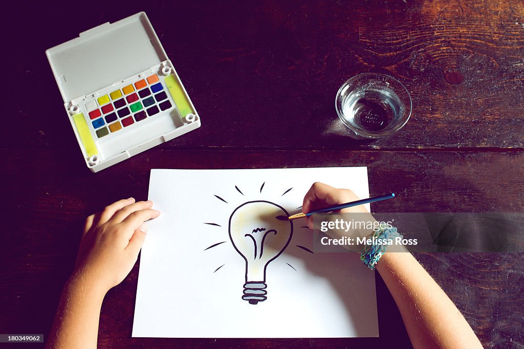 Child's hands painting a picture of a light bulb