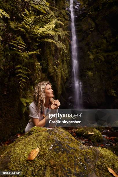 joven mujer despreocupada soñando despierta junto a la cascada en la naturaleza. - woman day dreaming fotografías e imágenes de stock