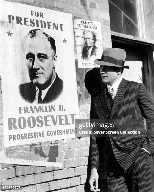 American actor Warren Beatty, as Clyde Barrow, posing next to a Roosevelt campaign poster in a promotional portrait for 'Bonnie And Clyde', directed...