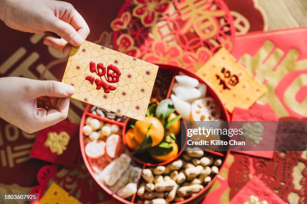 woman holding a chinese new year red envelop with candy box full of traditional chinese snack on the background - capodanno cinese foto e immagini stock