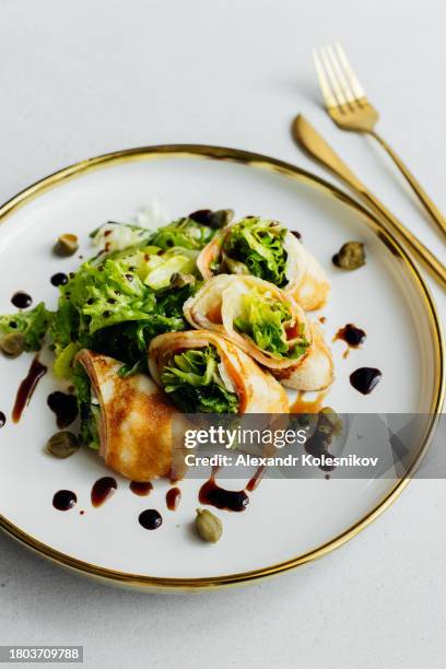 rolls of thin pancakes with salmon fish and lettuce greens on plate on stone light table. delicious and healthy breakfast - maslenitsa stock pictures, royalty-free photos & images