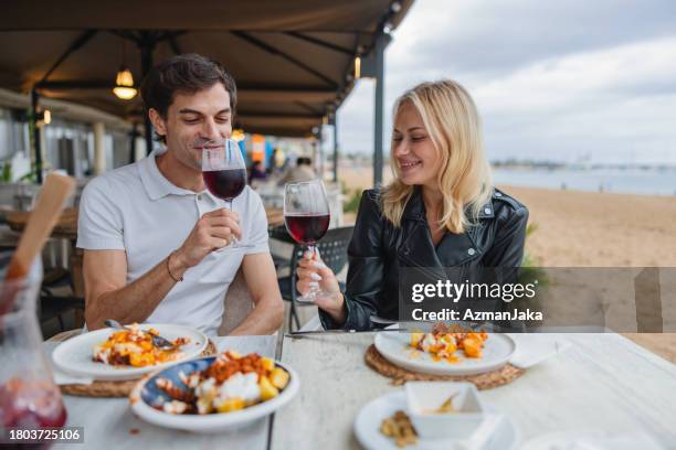 international couple enyoying a glass of red wine together at a restaurant outside at the beach - patatas bravas stockfoto's en -beelden