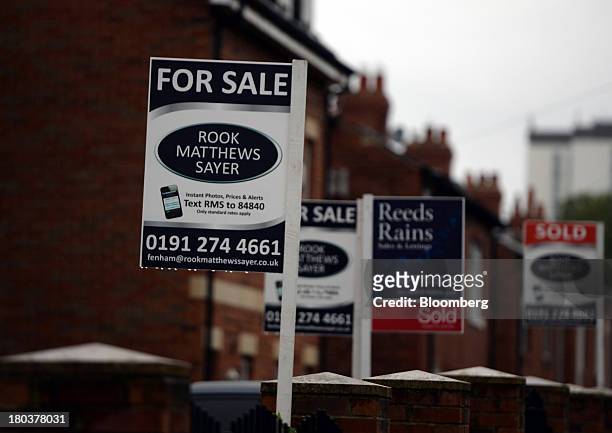 Estate agents' "For Sale" and "Sold" signs stand in the rain in front of a row of terraced residential houses in Newcastle-upon-Tyne, U.K., on...