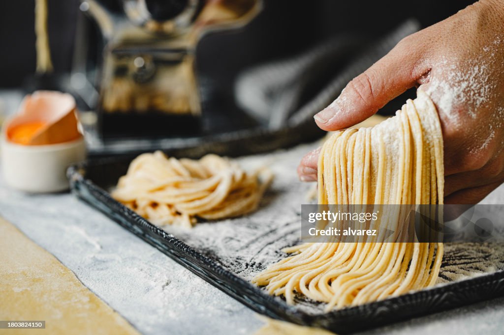 Primer plano de la mujer que hace pasta de espagueti con masa en la mesa de la cocina