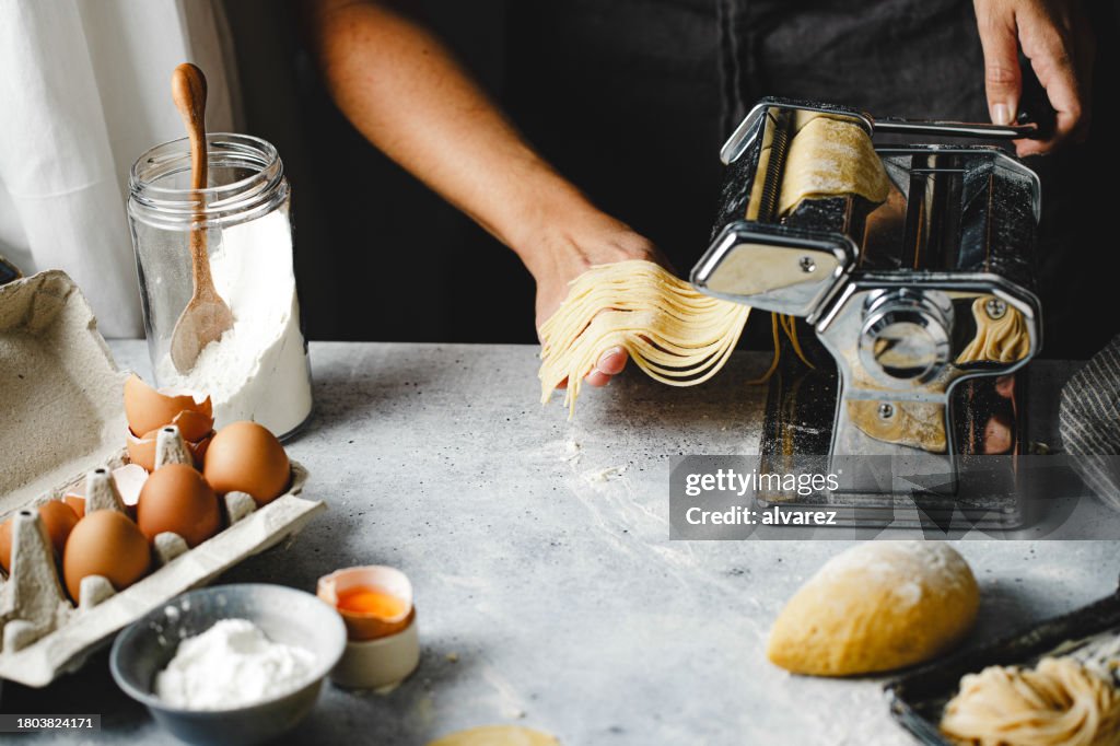 Nahaufnahme einer Frau, die zu Hause mit einer Maschine hausgemachte Nudeln herstellt