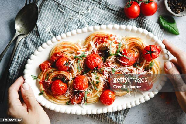 top view of woman hands holding a plate of freshly prepared spicy tomato basil pasta - tomatenpasta stockfoto's en -beelden