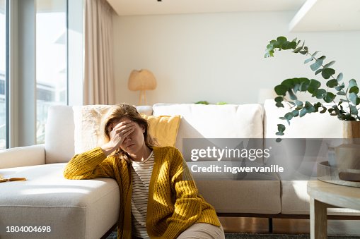 Woman having headache and holding her head while sitting on the floor at home Woman having headache and holding her head while sitting on the floor at home