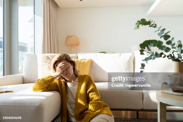 woman having headache and holding her head while sitting on the floor at home - orolig bildbanksfoton och bilder