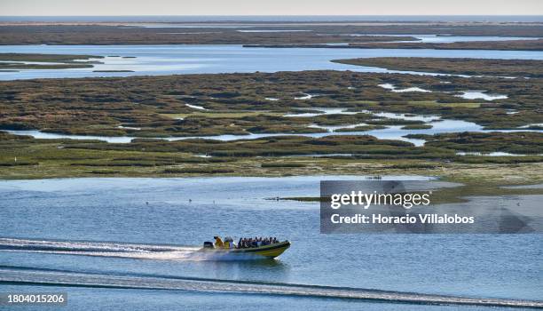 Fast motorboat with tourists sailing Ria Formosa lagoon seen from the terrace of the Old Beer Factory, a cultural and tourist attraction, at the end...