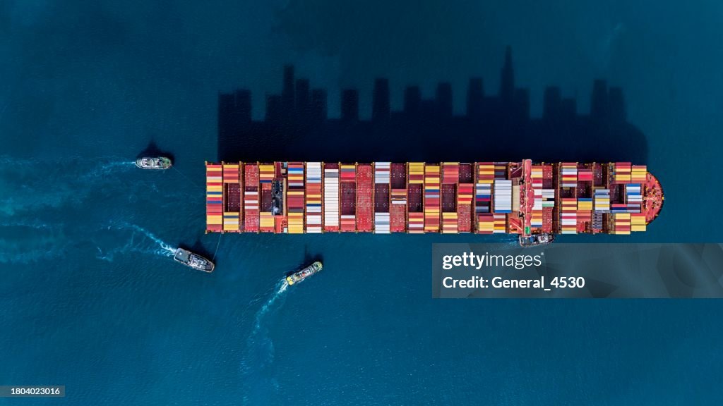 Aerial top view tugboat sailing alongside container ship at blue sea.