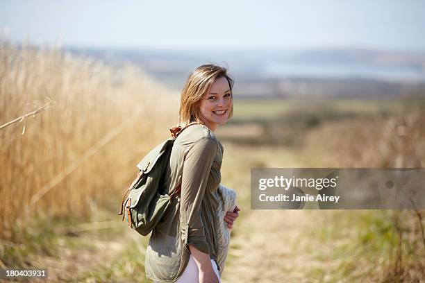 portrait of young woman on dirt track next to field of reeds - woman on walking in countryside stock pictures, royalty-free photos & images