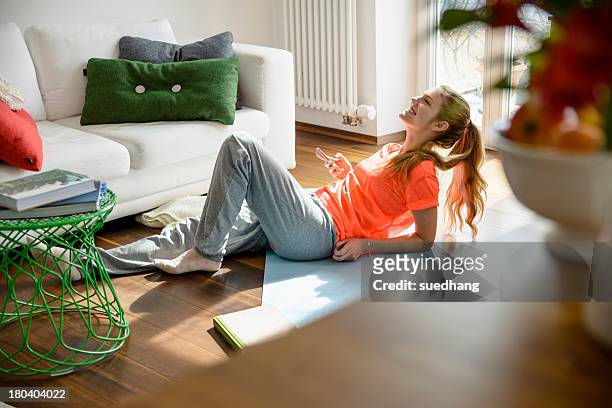 young woman holding smartphone whilst lounging on floor - jogging pants 個照片及圖片檔