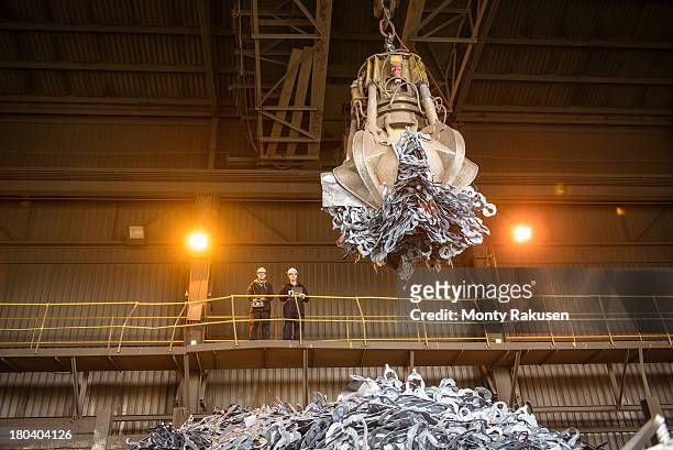 Low angle view of workers watching scrap metal grab in steel foundry