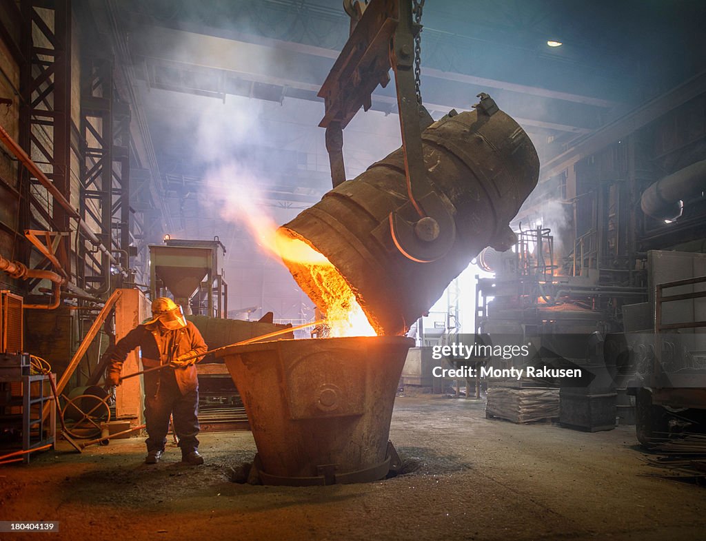 Steel worker cleaning large ladle in an industrial foundry
