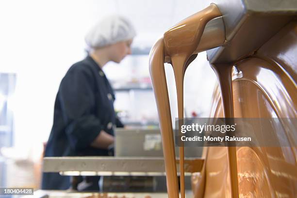 chocolatier in background as chocolate pours from machine in chocolate factory - close up of chocolates for sale stock pictures, royalty-free photos & images