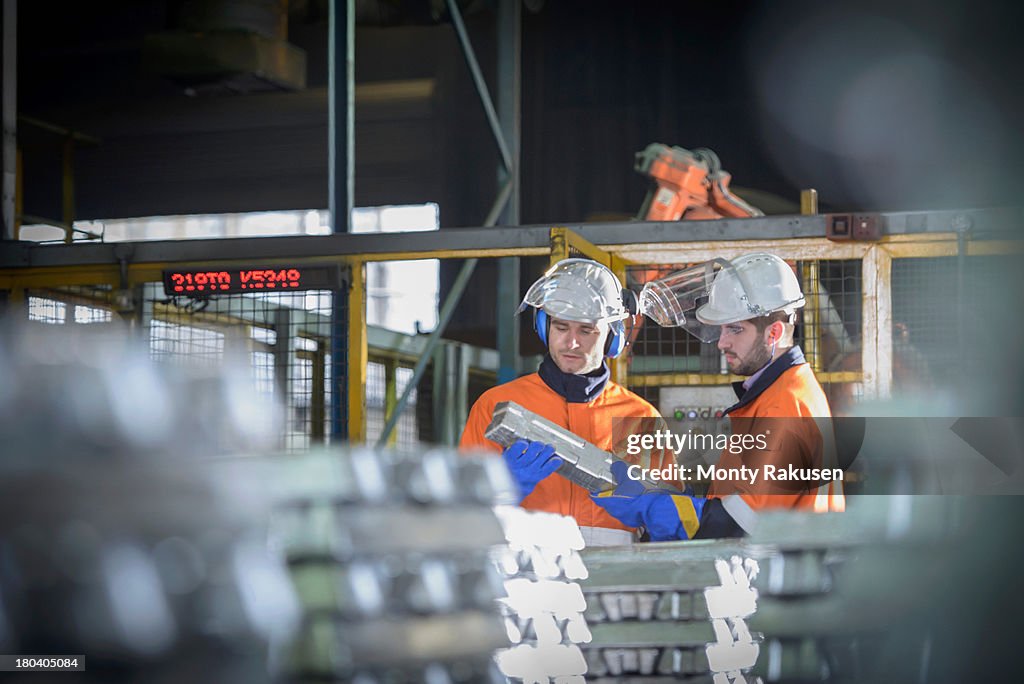 Workers in protective workwear inspecting aluminium ingot in foundry