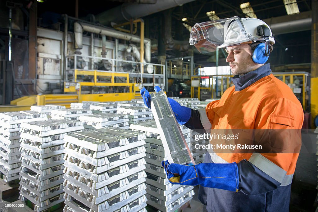 Worker in protective workwear inspecting aluminium ingot in foundry