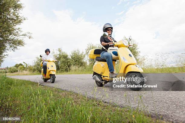 couple on scooters riding down rural road - moped stock-fotos und bilder