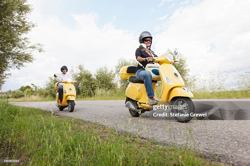 Couple on scooters riding down rural road