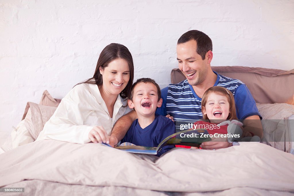 Parents and two young children looking at picture book in bed