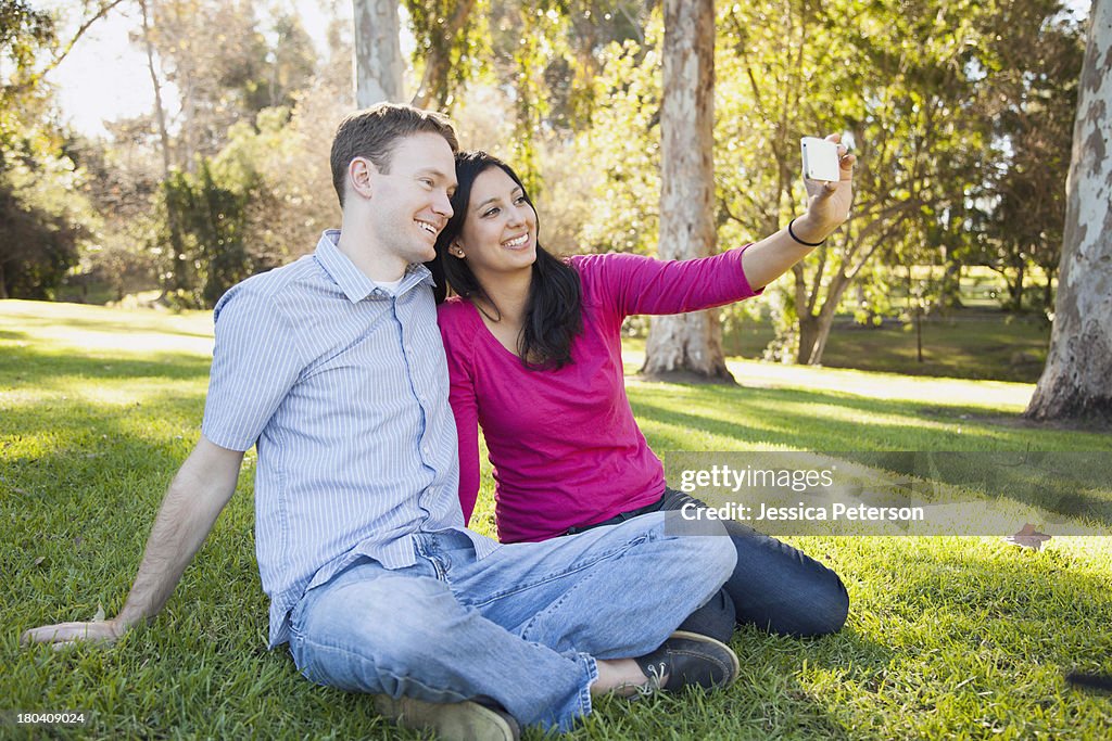 USA, California, Irvine, Couple sitting on grass in park photographing themselves