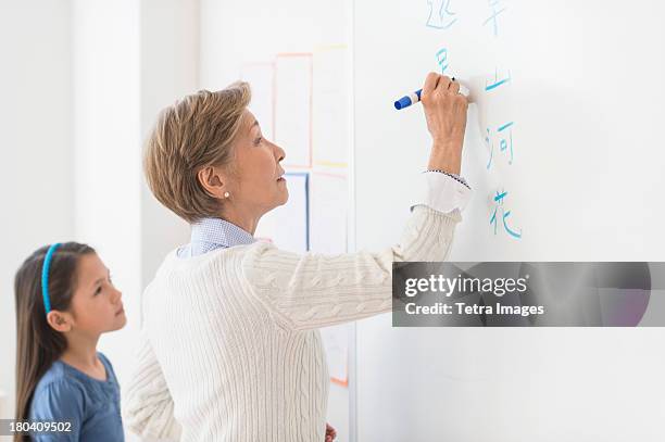 usa, new jersey, jersey city, teacher and schoolgirl (8-9) writing at whiteboard - tetra images teacher stock pictures, royalty-free photos & images