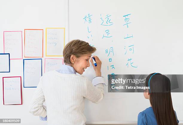 usa, new jersey, jersey city, teacher and schoolgirl (8-9) writing at whiteboard - tetra images teacher stock pictures, royalty-free photos & images