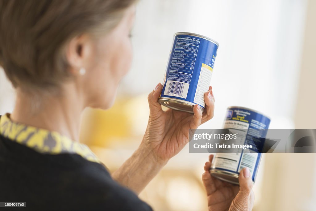 USA, New Jersey, Jersey City, Senior woman reading labels on canned food