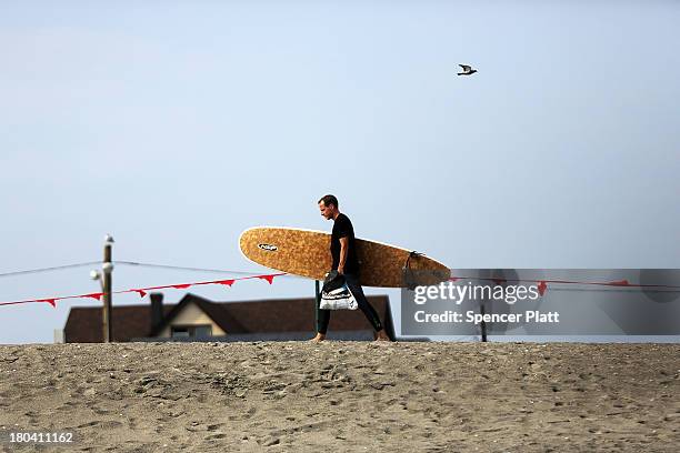 Man walks with his surfboard in the late afternoon at Rockaway Beach on September 12, 2013 in the Queens borough of New York City. Despite the...