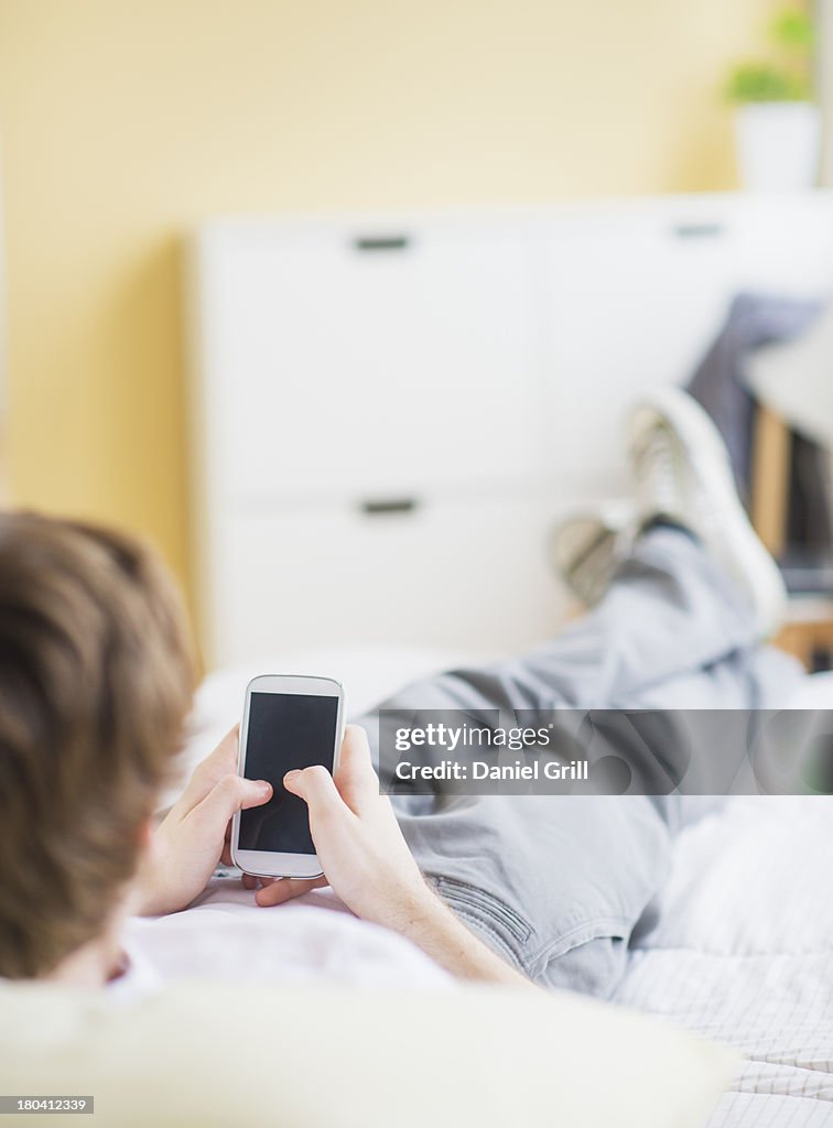 USA, New Jersey, Jersey City, Teenage boy (14-15) lying on bed and text messaging