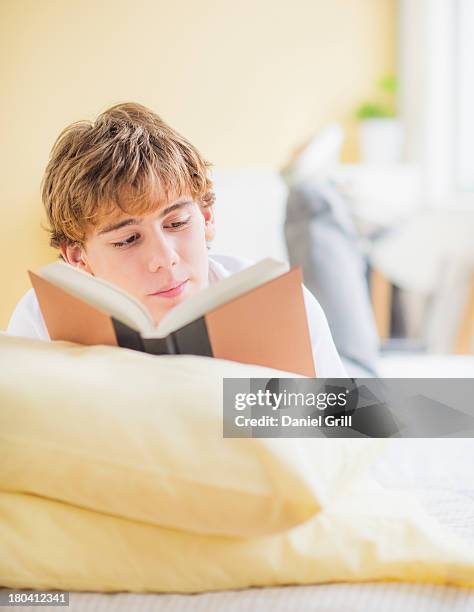 usa, new jersey, jersey city, teenage boy (14-15) lying on bed and reading book - boy reading a book stock-fotos und bilder