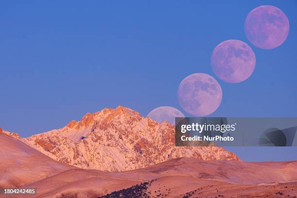 Image is a composition of 4 interval timer photos to show moon rising path) Beaver full moon rising above Monte Prena Mountain is seen from L'Aquila,...