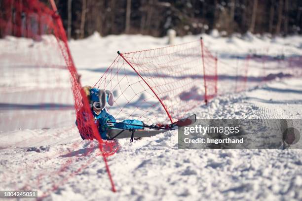 smiling little boy catched by the ski slope safety net after crashing during ski lesson - safety net stock pictures, royalty-free photos & images